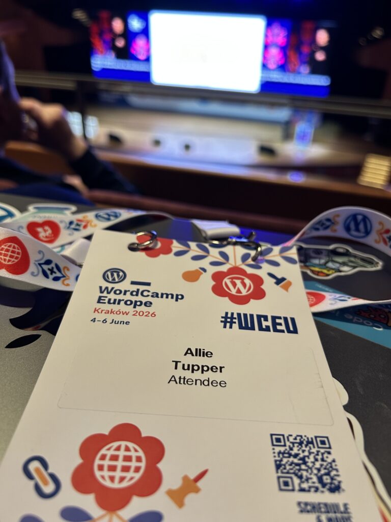 A WordCamp Europe 2026 Attendee badge sits on a MacBook in a darkened auitorium